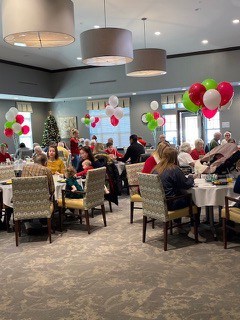 elderly residents of a senior living community sitting with their family members at tables with balloons attached at an event
