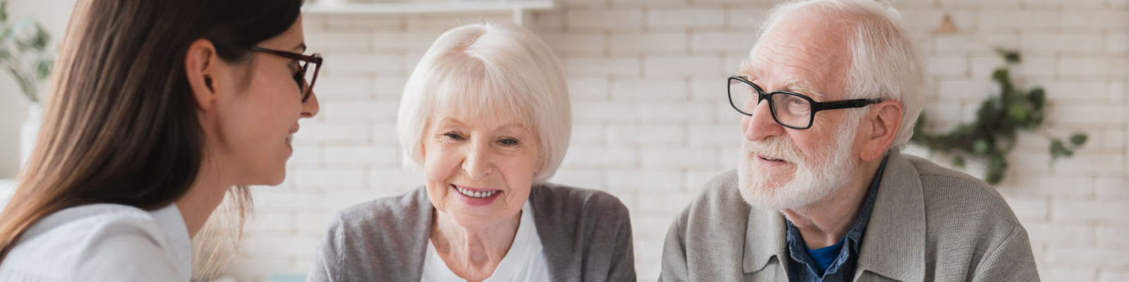 A senior man and woman sitting together at a table across from a female insurance specialist