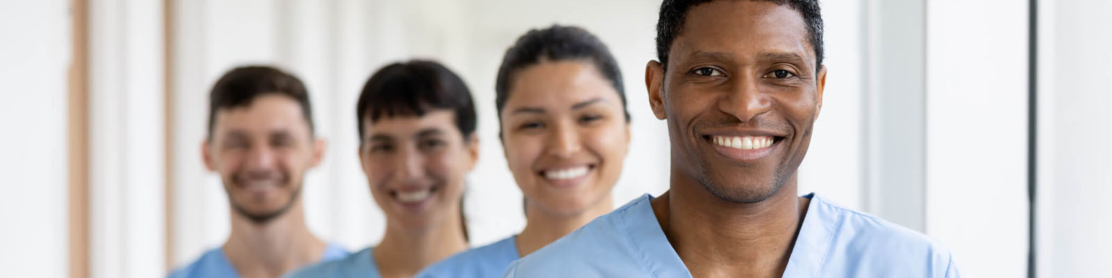 Four senior living employees standing in a staggered line smiling and wearing blue scrubs