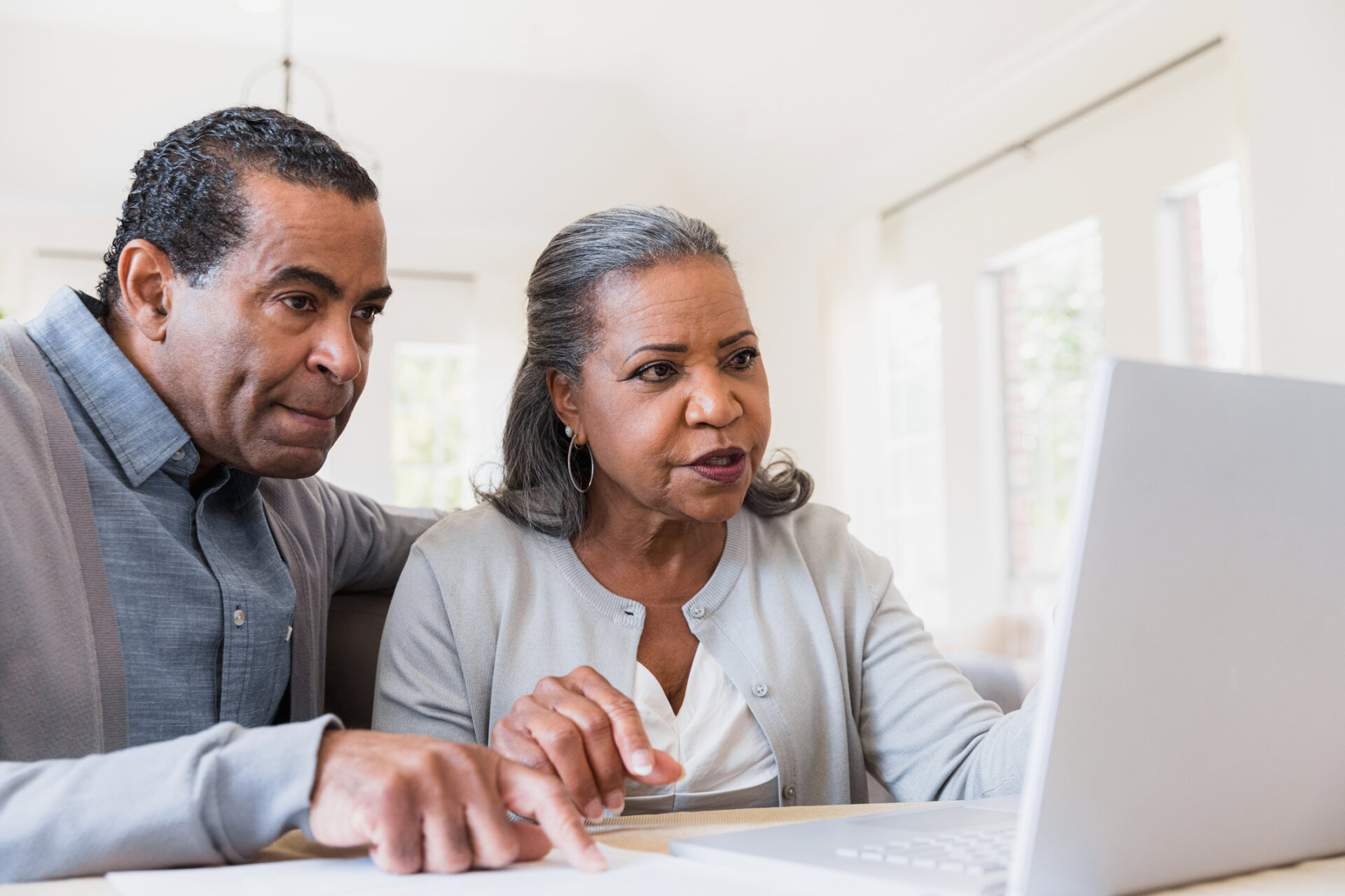 Senior man and woman sitting at their kitchen table looking at Park Place Senior Living information on a laptop