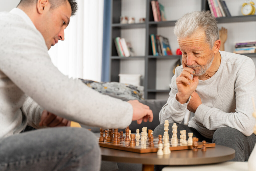 Senior memory care resident sitting in his apartment playing chess with his son at Park Place Senior Living