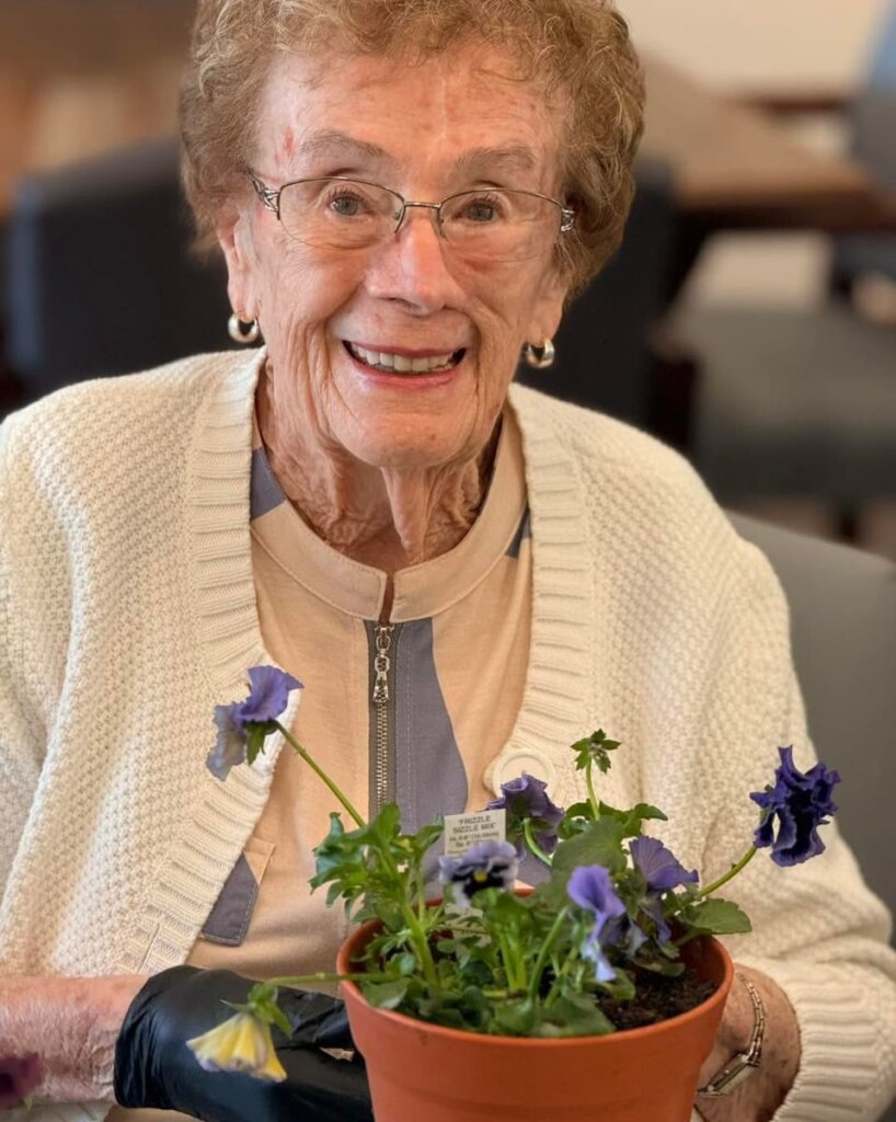 A delighted resident holds a freshly potted arrangement of purple violas during a flower planting activity at Park Place Senior Living.