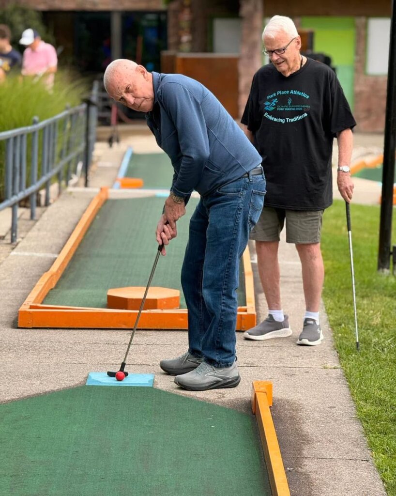 Two residents enjoy a round of mini golf on an outdoor course during a Park Place Senior Living community outing.