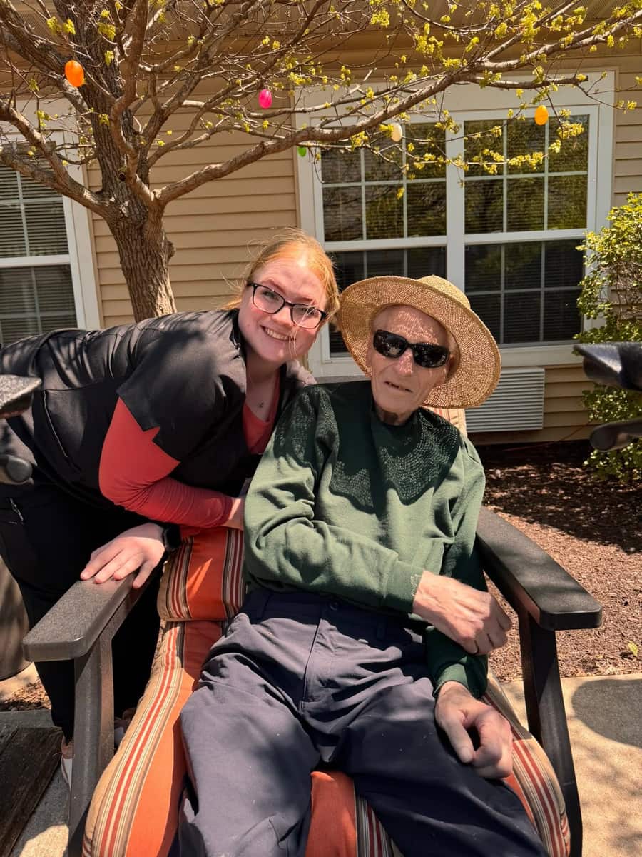A Park Place team member sits with a resident in Adirondack chairs on the outdoor patio on a sunny spring day.